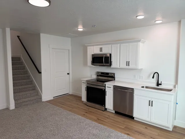 Compact kitchen area featuring white cabinetry, stainless steel appliances, a single-basin sink with a matte black faucet, and light-toned wood-finish flooring