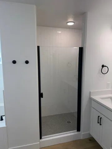 Walk-in shower with black-framed glass enclosure, white rectangular subway tile surround, and black penny tile flooring
