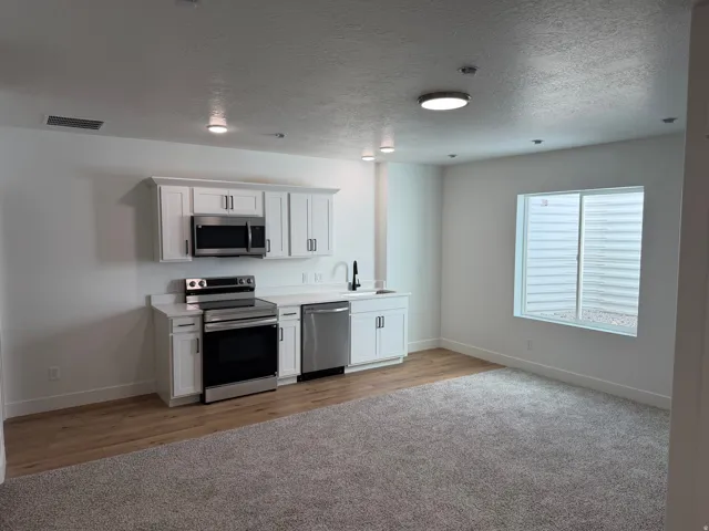 Open-concept living area featuring a kitchen with white cabinetry, stainless steel appliances, and light-colored countertops