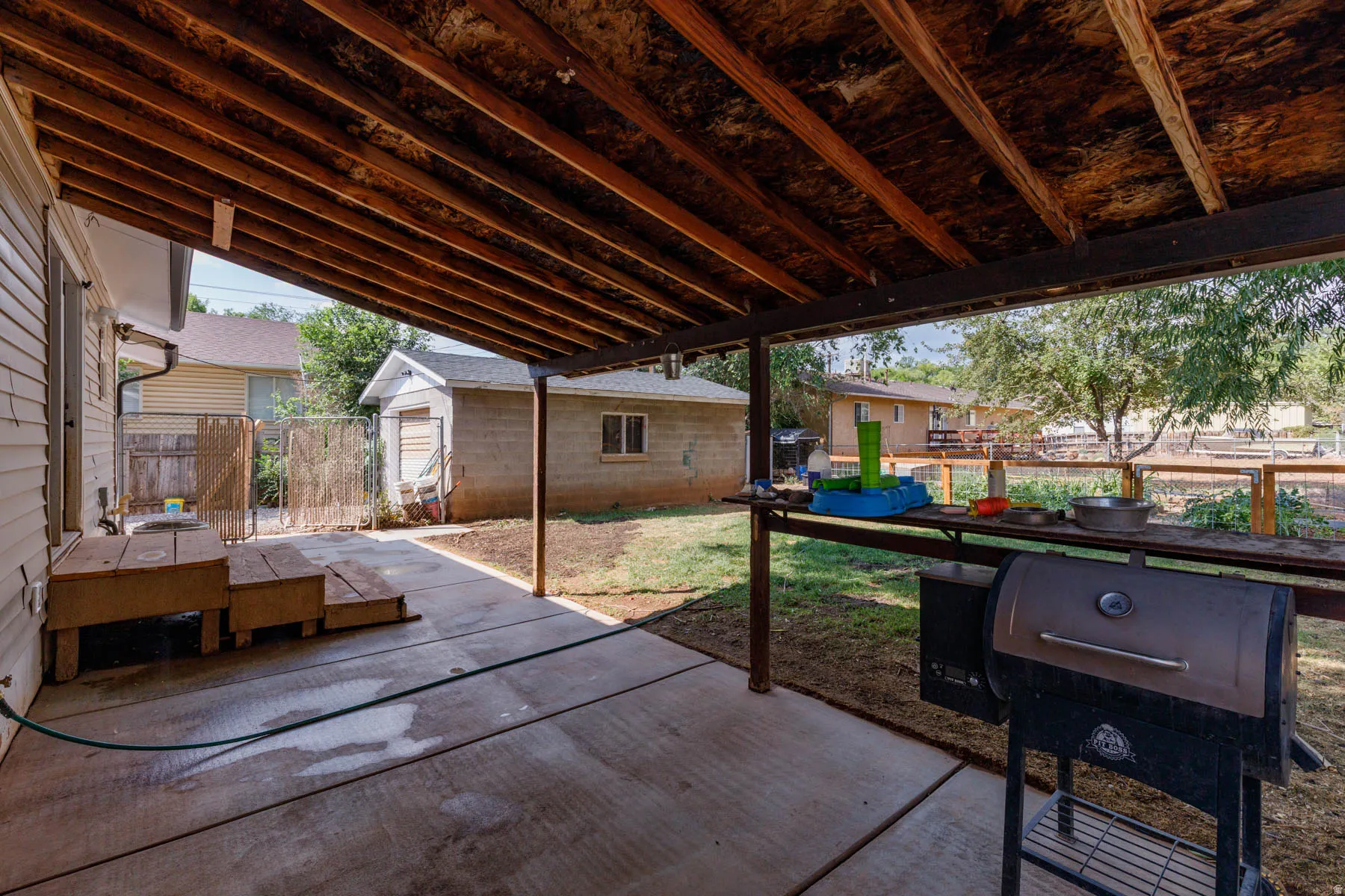 Expansive covered patio featuring a concrete surface, exposed wood rafters, and a built-in counter space