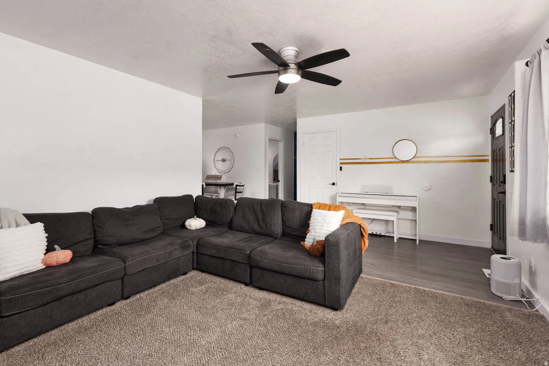 Living room featuring wood-finish flooring, a ceiling fan with integrated lighting, and a white interior door with black hardware