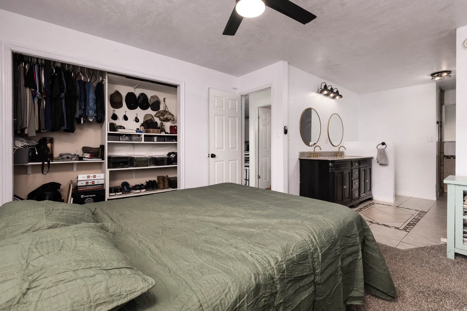 Bedroom featuring a ceiling fan, carpet flooring, built-in closet organization, and an en-suite vanity with dual oval mirrors and a dark wood-finish cabinet