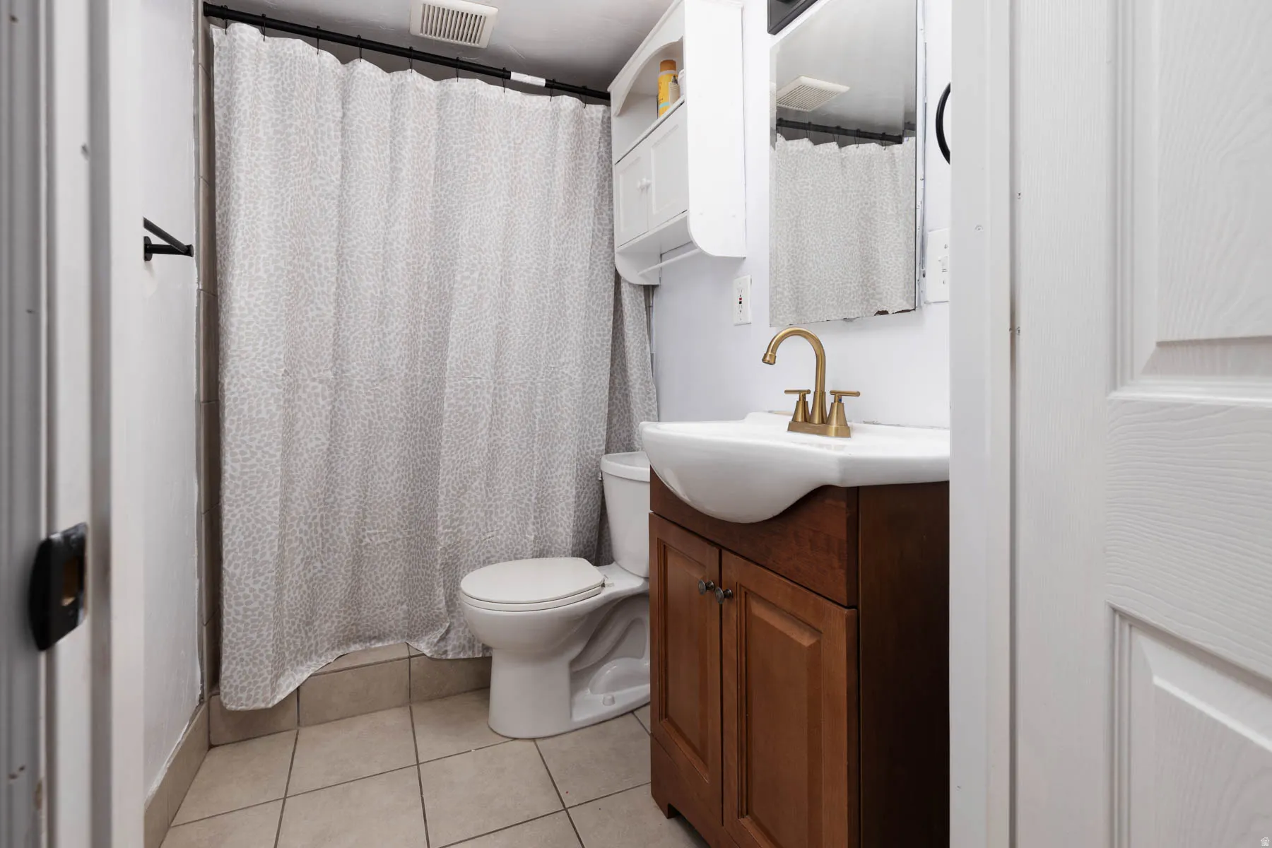 Full bathroom featuring a single vanity with wood-finish cabinetry, a vessel sink with a brass-finish faucet, and a wall-mounted mirror
