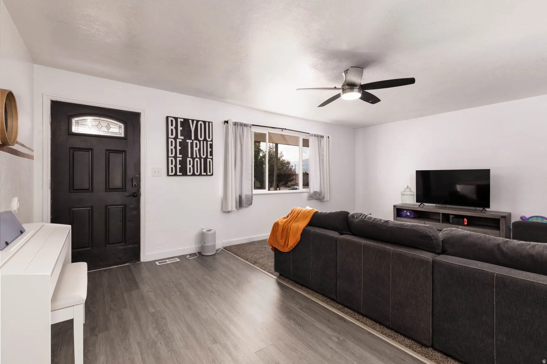 Light-filled living area featuring wood-finish flooring, a contemporary ceiling fan, and a prominent window