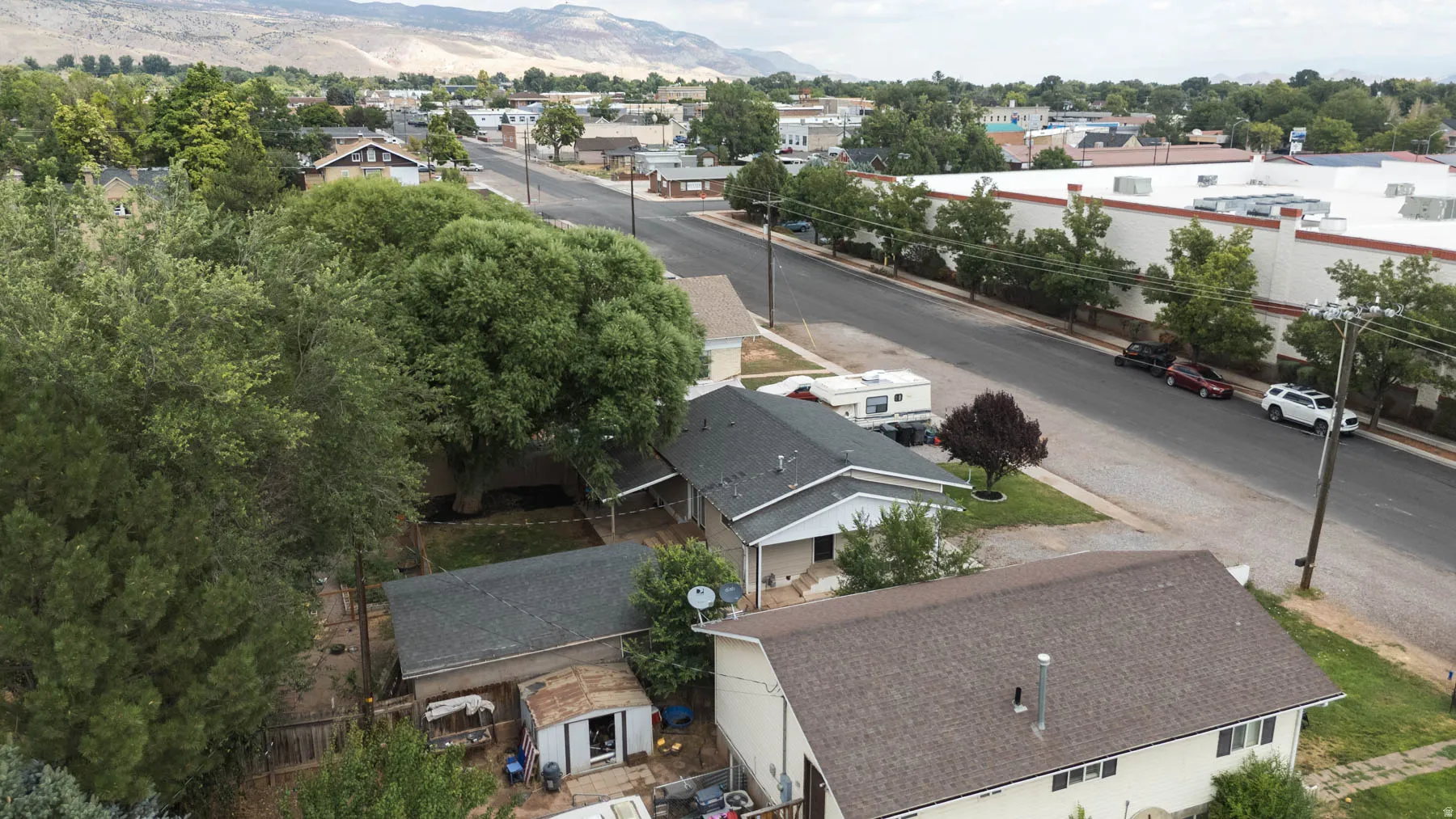 Rooftop perspective showcasing multiple properties with mature trees, a paved street, and distant mountain scenery