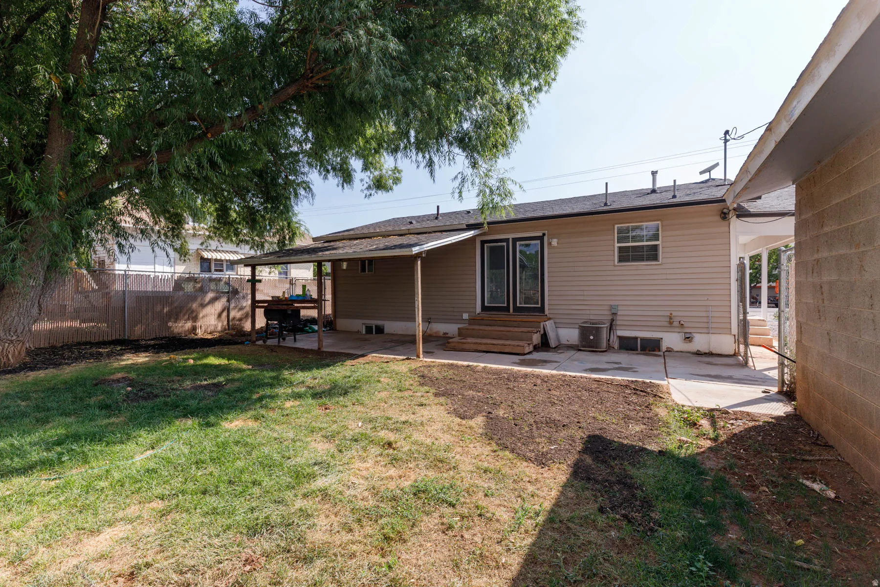 Expansive backyard featuring a large mature tree, a covered patio area, and a concrete patio