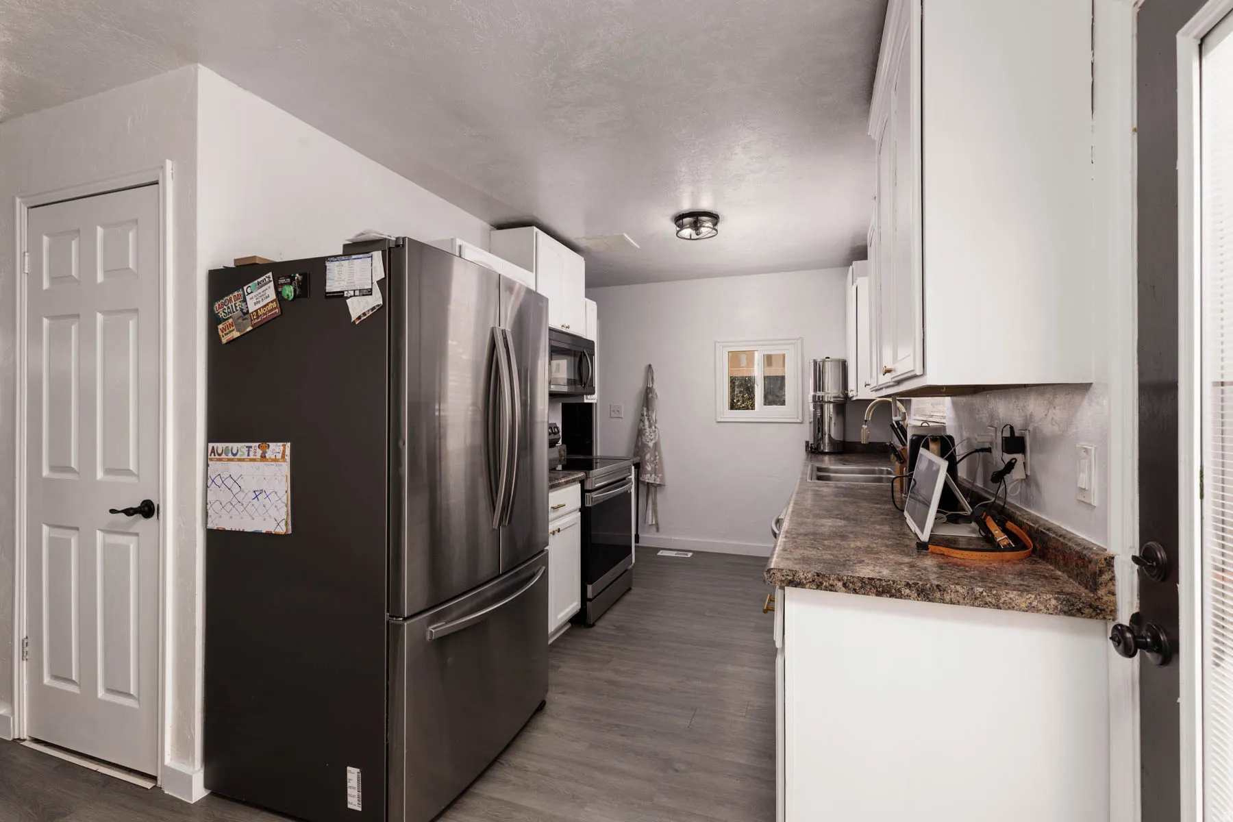 Galley kitchen featuring wood-finish flooring, white cabinetry, dark countertops, and stainless steel appliances