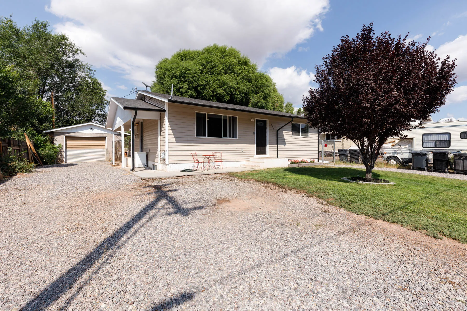 Exterior featuring light-colored siding, a covered porch entry, a gravel driveway, an attached garage, and a mature tree