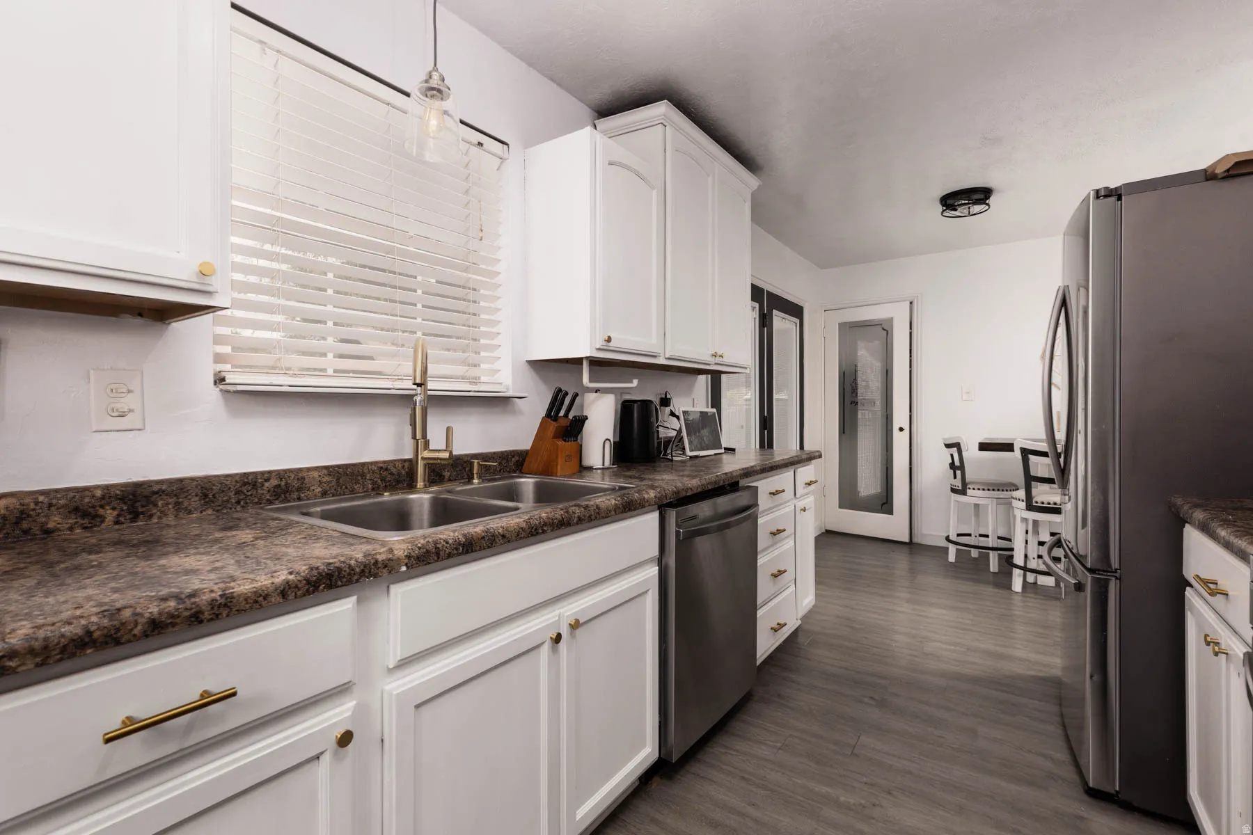 Kitchen featuring white cabinetry with gold-finish hardware, a double basin stainless steel sink with a gold-finish faucet, dark patterned countertops, and wood-finish flooring