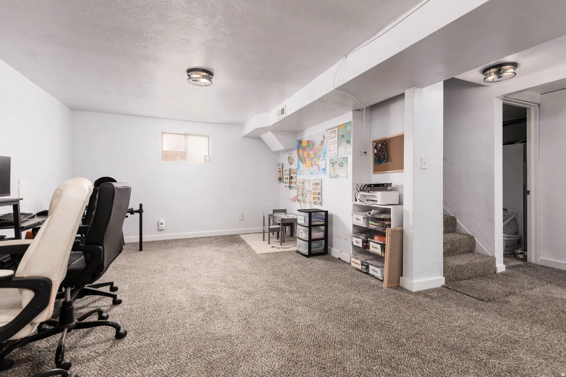 Finished lower level featuring neutral carpeting, recessed window, exposed ceiling beams, and a carpeted staircase