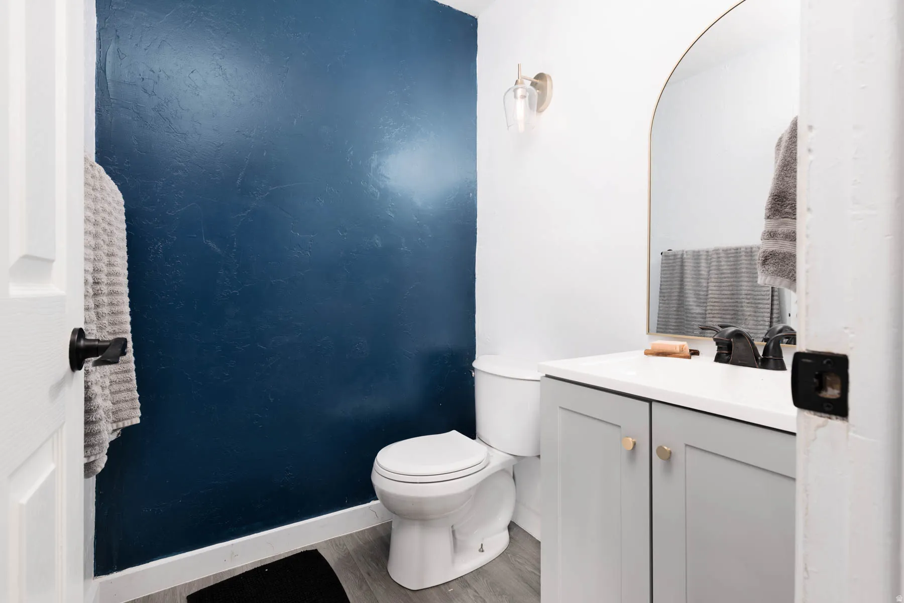 Bathroom featuring a white toilet, gray vanity with gold-toned hardware, solid-surface countertop, and a matte black faucet