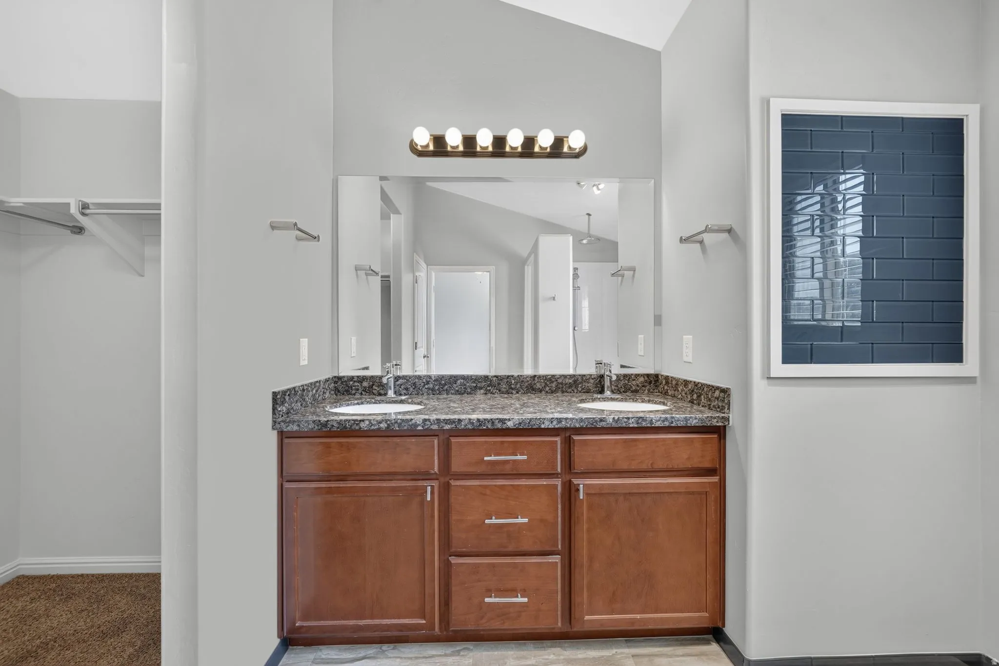 Double vanity featuring a granite-style countertop with two undermount sinks, wood-finish cabinetry, and a full-width mirror