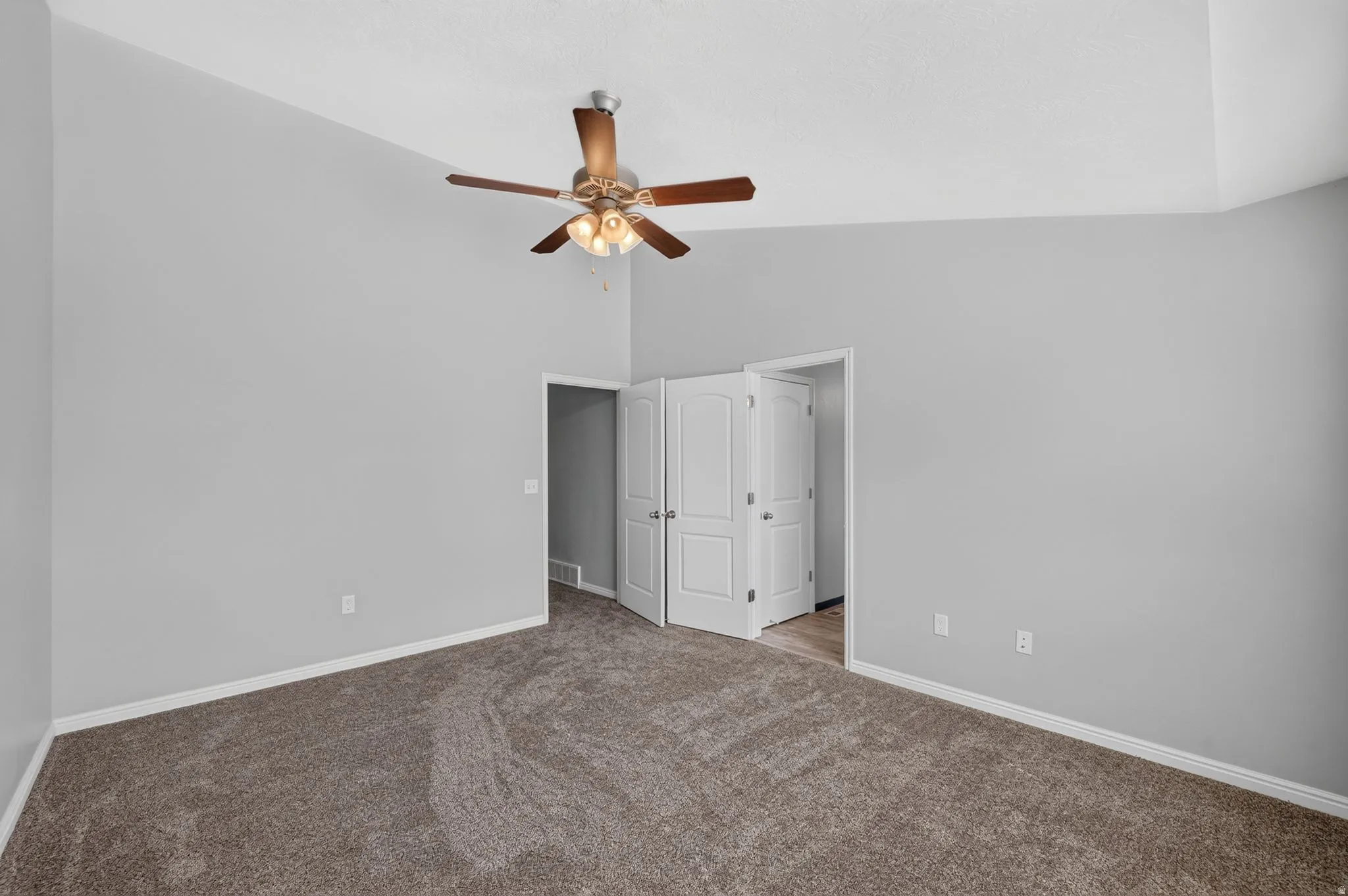 Spacious room featuring textured carpet flooring, vaulted ceilings, and a ceiling fan with integrated lighting