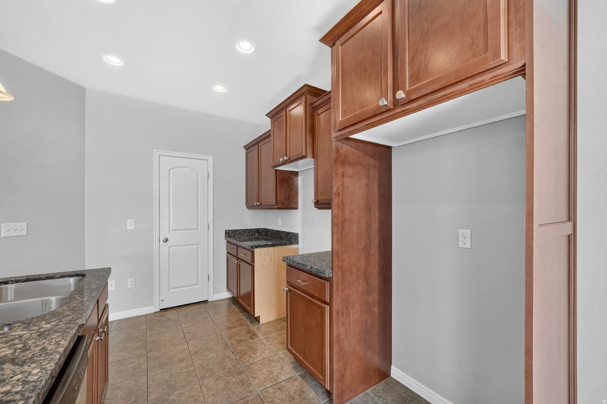 Kitchen featuring wood cabinetry, dark speckled countertops, a stainless steel double basin sink, and recessed lighting