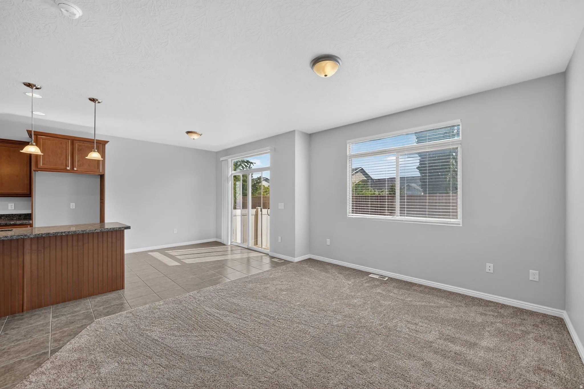 Open-concept living space featuring a breakfast bar with pendant lighting, wood-finish cabinetry, tile flooring, and sliding glass door access to the exterior