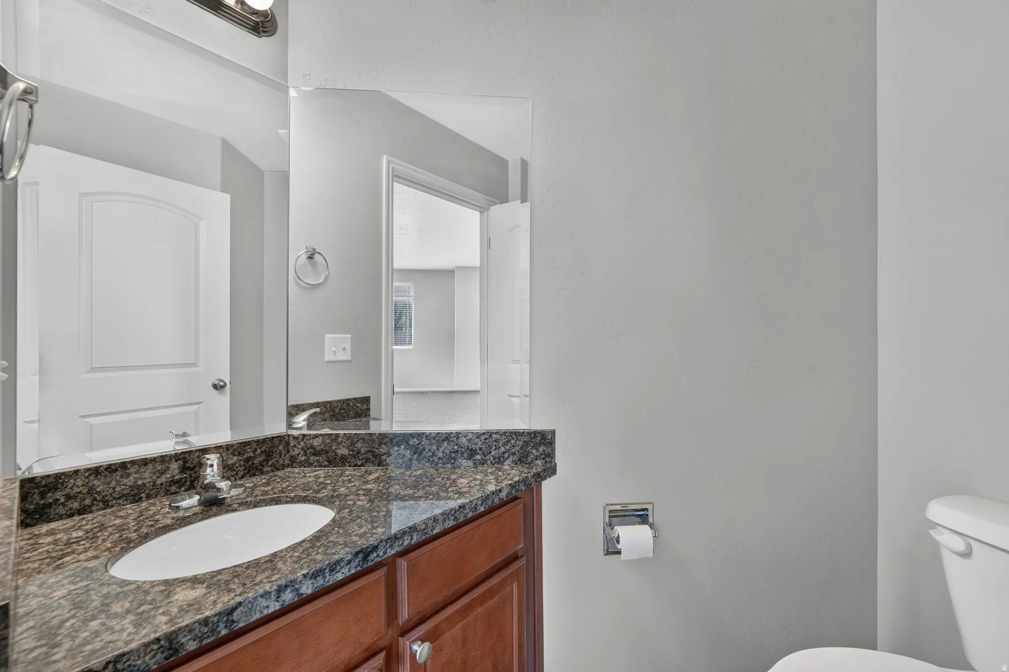 Bathroom vanity featuring a dark granite countertop with an undermount sink, wood-finish cabinetry, and a chrome faucet