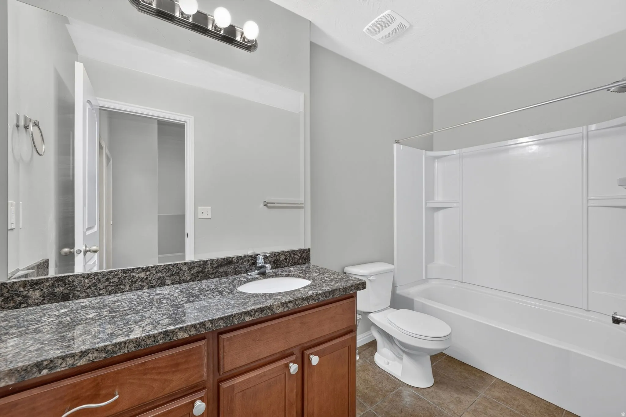 Bathroom featuring a wood-finish vanity with a built-in sink, a speckled countertop, a large mirror, a chrome light fixture, and a white tub/shower combination