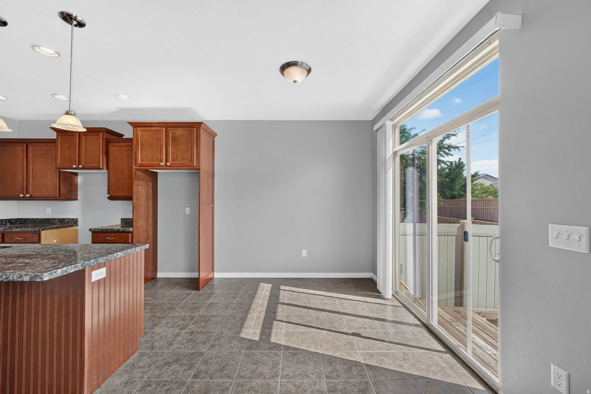 Kitchen and dining area featuring warm wood cabinetry, a central island with a speckled countertop, and tiled flooring