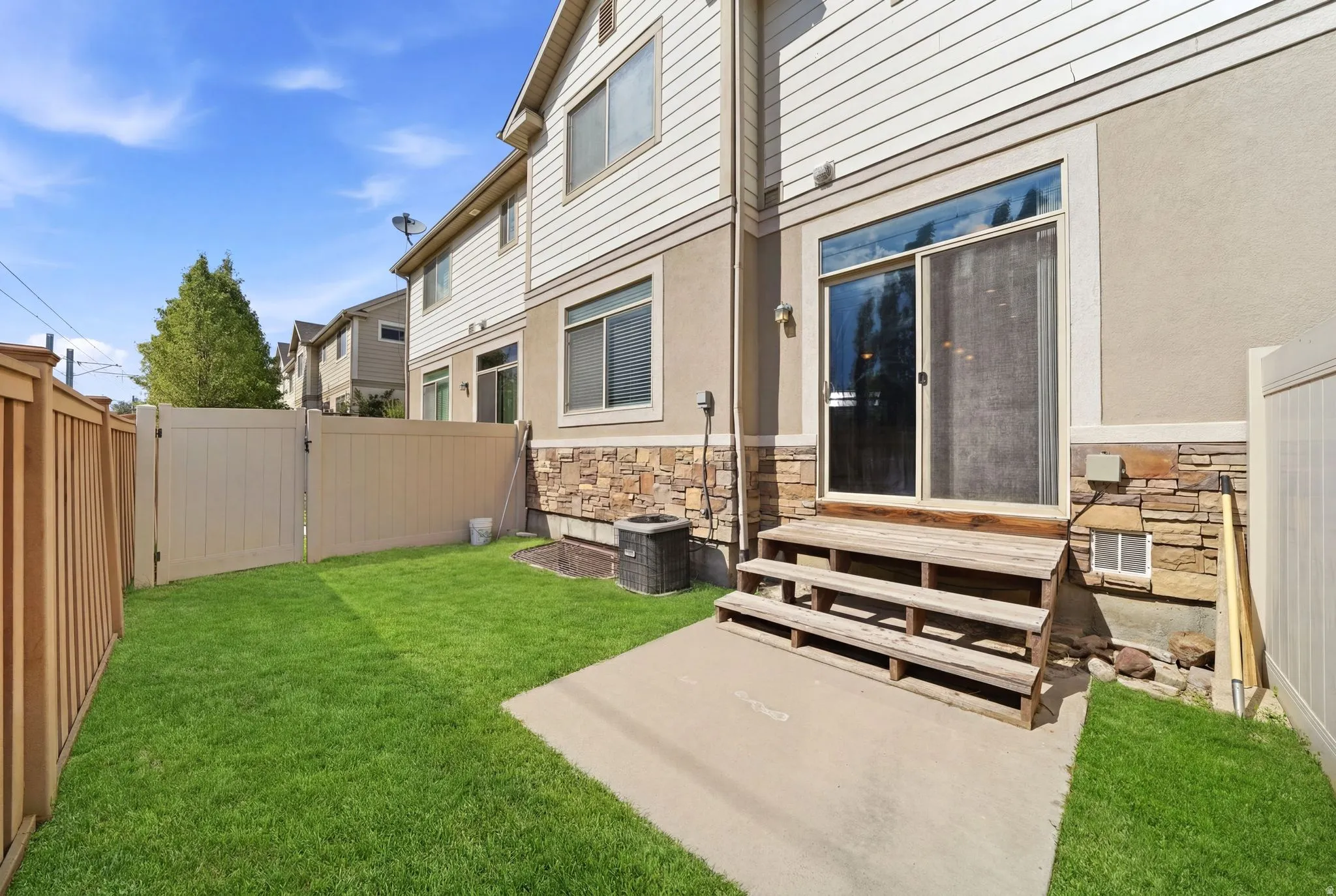 Private fenced backyard with a patio, green lawn, and a light beige vinyl fence