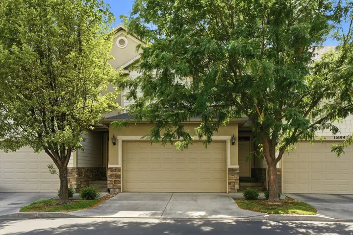 Multi-level stucco exterior featuring stone accents, a two-car garage, and established trees