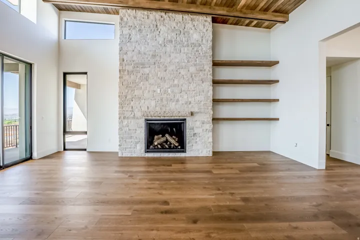 Wood-finish flooring, stone fireplace with hearth, built-in shelving, wood-beam ceiling, and sliding glass door to exterior