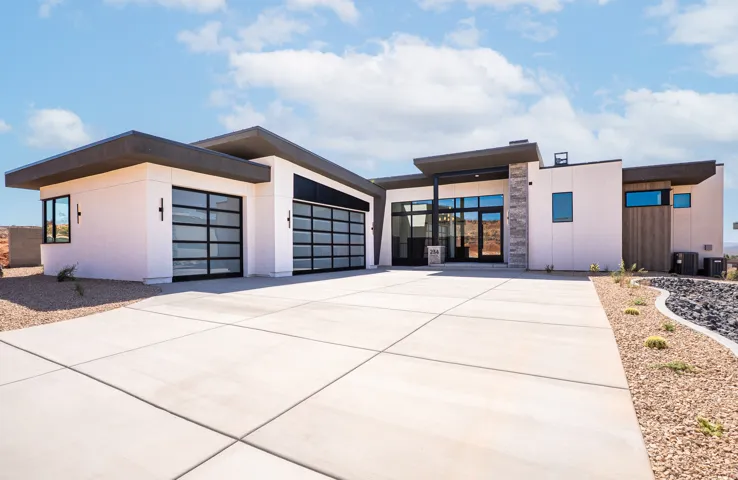 Modern exterior with a flat roofline, stone cladding accents, large glass panel garage doors, and a concrete driveway