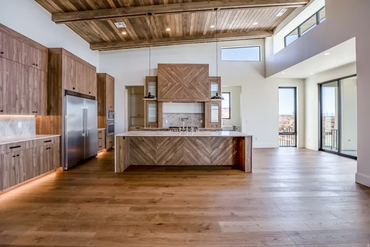 Spacious open-concept interior featuring wood-finish flooring, vaulted wood-plank ceiling, and an expansive kitchen with wood cabinetry, large island, and stainless steel appliances