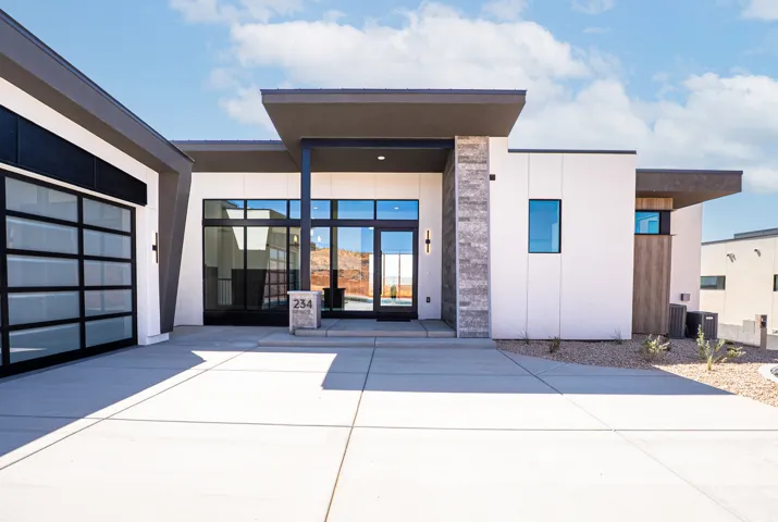 Modern architectural design featuring a flat roofline, glass panel garage door, stone accent pillar, recessed entry, and large format windows