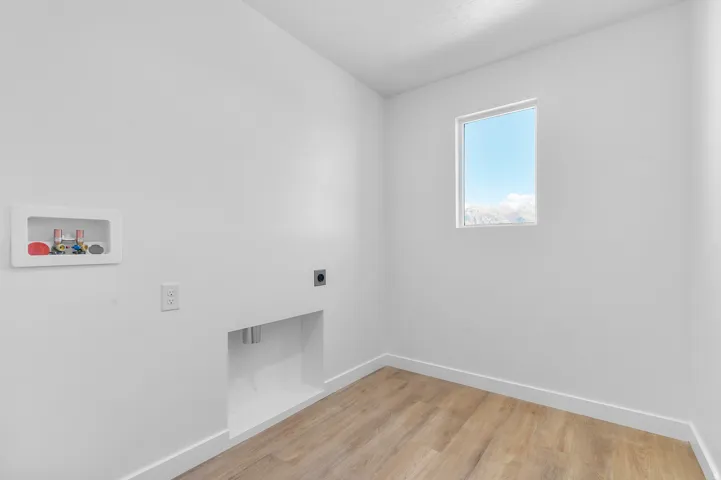 Laundry area featuring wood-finish flooring, white walls, and a window providing natural light