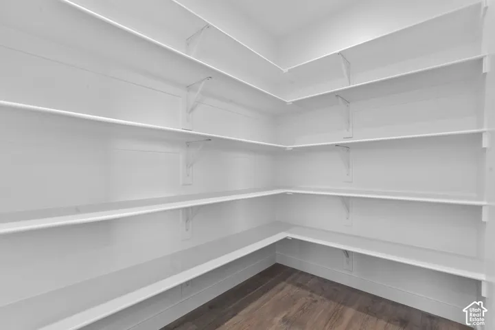 Corner pantry featuring multiple white built-in shelves, white walls, and wood-finish flooring