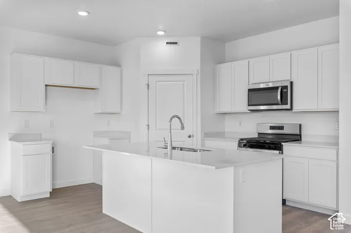 Modern kitchen featuring white cabinetry, light-toned countertops, a stainless steel gas range, and a central island with an integrated sink
