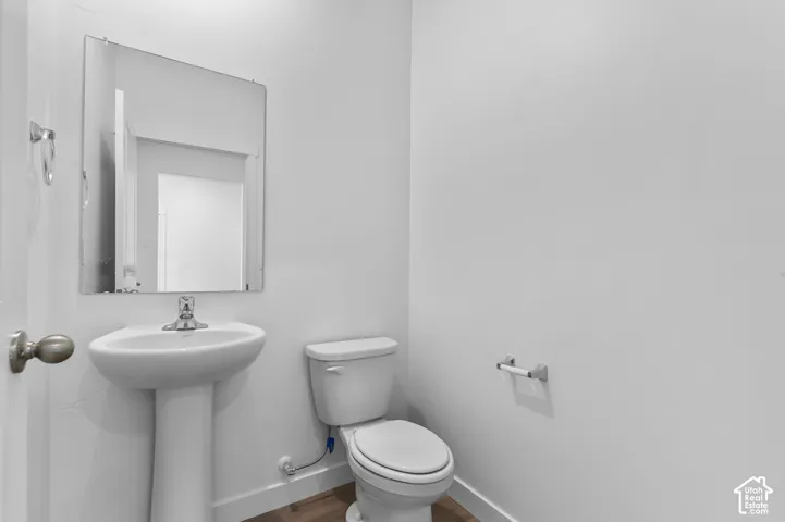 White pedestal sink with chrome faucet, wall-mounted mirror, and wood-finish flooring