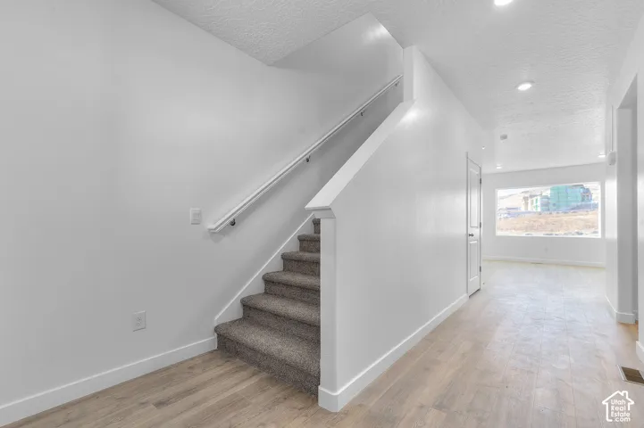 Bright entry hall featuring wood-finish flooring, a carpeted staircase with white handrail, recessed lighting, and a large window