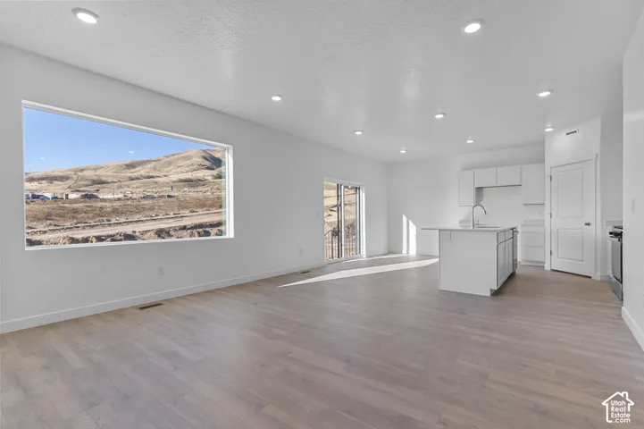 Open-concept living area featuring light wood-finish flooring, recessed lighting, and a large picture window showcasing the natural landscape
