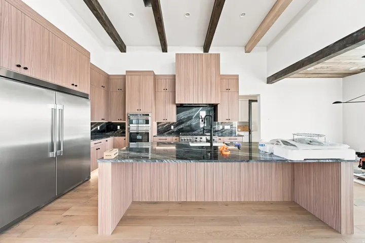 Gourmet kitchen featuring wood-finish cabinetry, a large kitchen island with a dark stone countertop, stainless steel appliances, and exposed ceiling beams