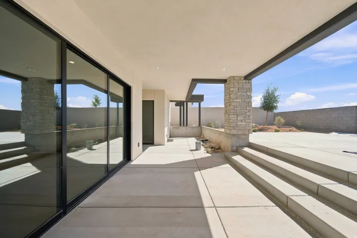 Expansive concrete patio featuring a covered area with recessed lighting, stone-clad support columns, and large sliding glass doors