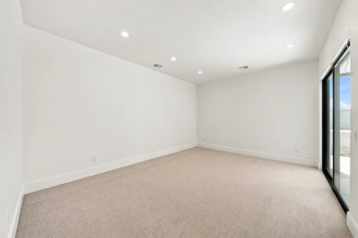 Recessed lighting, light neutral carpeting, white walls, and a large sliding glass door