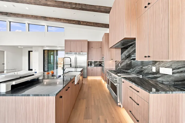 Gourmet kitchen featuring light wood-finish cabinetry, dark stone countertops, stainless steel appliances, and wood-finish flooring