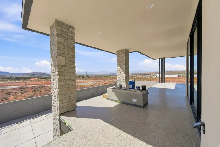 Expansive covered patio featuring stone-clad columns, recessed lighting, and a built-in outdoor counter