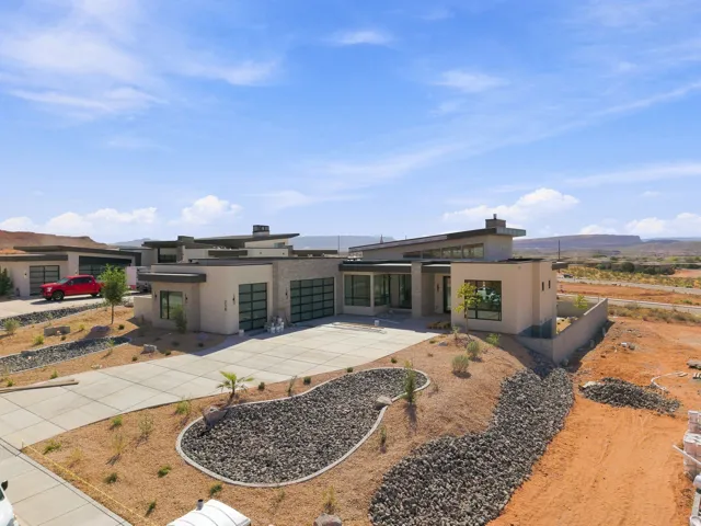 Modern exterior architecture with a flat roofline, integrated garages with glass panel doors, a concrete driveway, and xeriscaped plantings