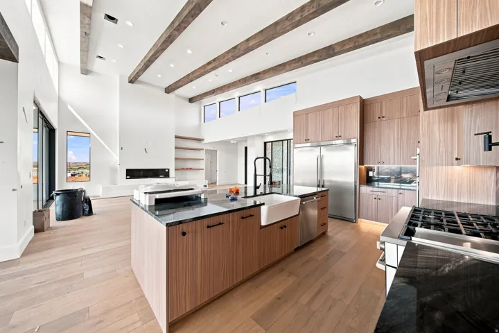 Vaulted ceilings with exposed wood beams, wood-finish flooring, built-in fireplace, full-height cabinetry, and a large kitchen island with integrated sink