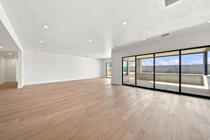Expansive interior with wood-finish flooring, recessed lighting, and large sliding glass doors opening to an outdoor patio