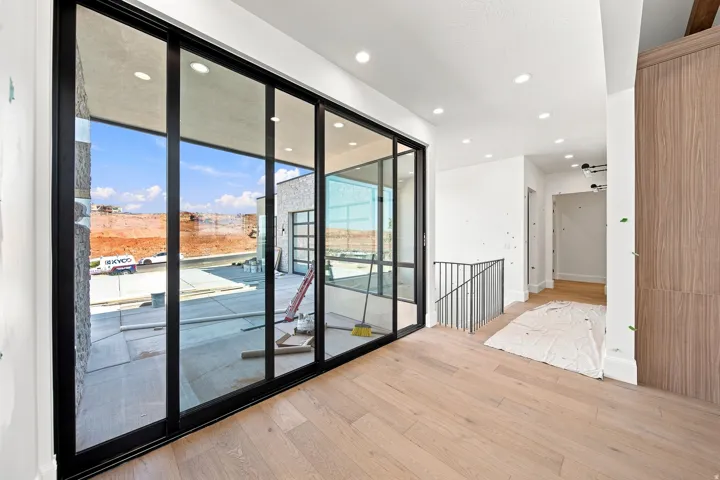 Expansive sliding glass doors, light wood-finish flooring, recessed ceiling lighting, a metal railing, and built-in wood-finish cabinetry