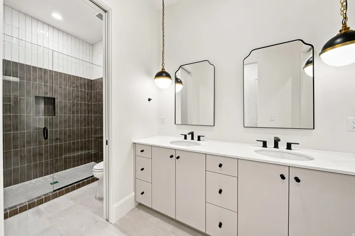 Dual vanity with white cabinetry and integrated sinks, matte black hardware and faucets, two framed mirrors, and pendant lighting