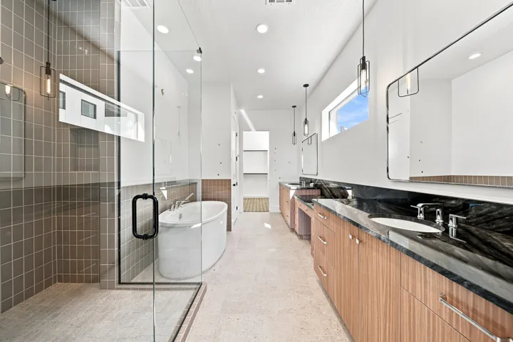 Spacious bathroom featuring a freestanding tub, glass-enclosed shower with tile surround, dual vanity with wood-finish cabinetry, and black stone countertops