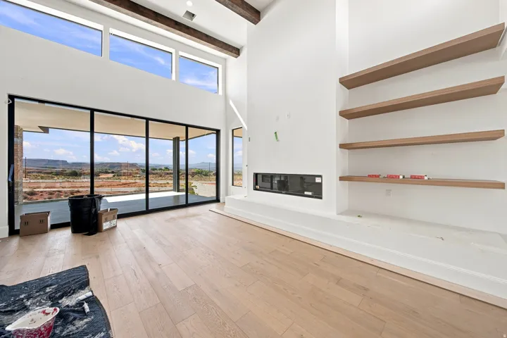 Expansive sliding glass doors, upper transom windows, exposed ceiling beams, wood-finish flooring, and a built-in fireplace feature with floating shelves