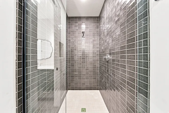 Walk-in shower with full-height gray tile, glass enclosure, and white tiled flooring