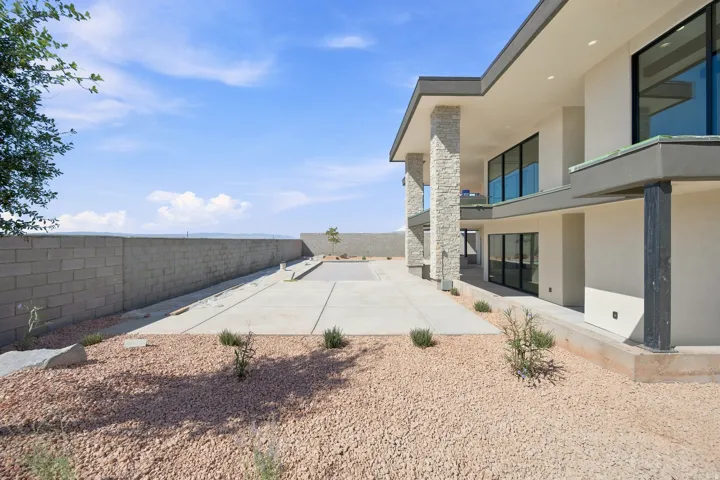 Modern architectural design with multiple large windows, stone-clad support columns, and an expansive concrete patio