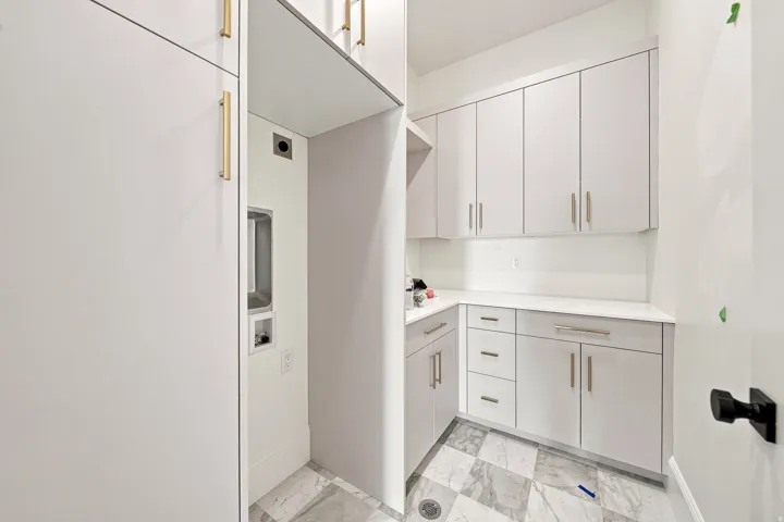 White shaker cabinetry, light-toned countertop, modern gold-finish hardware, and patterned tile flooring