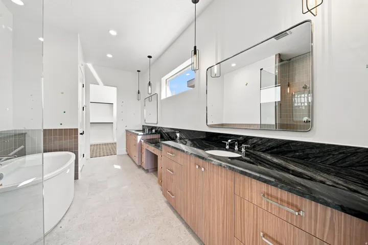 Dual wood-finish vanities with black stone countertops, undermount sinks, and chrome fixtures